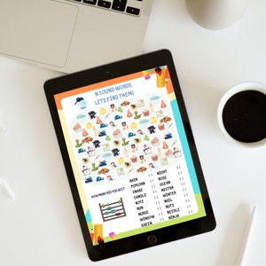 Puede incluir: Una tableta digital que muestra una hoja de actividades educativa titulada N SOUND WORDS LETS FIND THEM! La pantalla presenta una cuadr&iacute;cula de ilustraciones coloridas que incluyen ninjas, serpientes, narices y palomitas de ma&iacute;z.