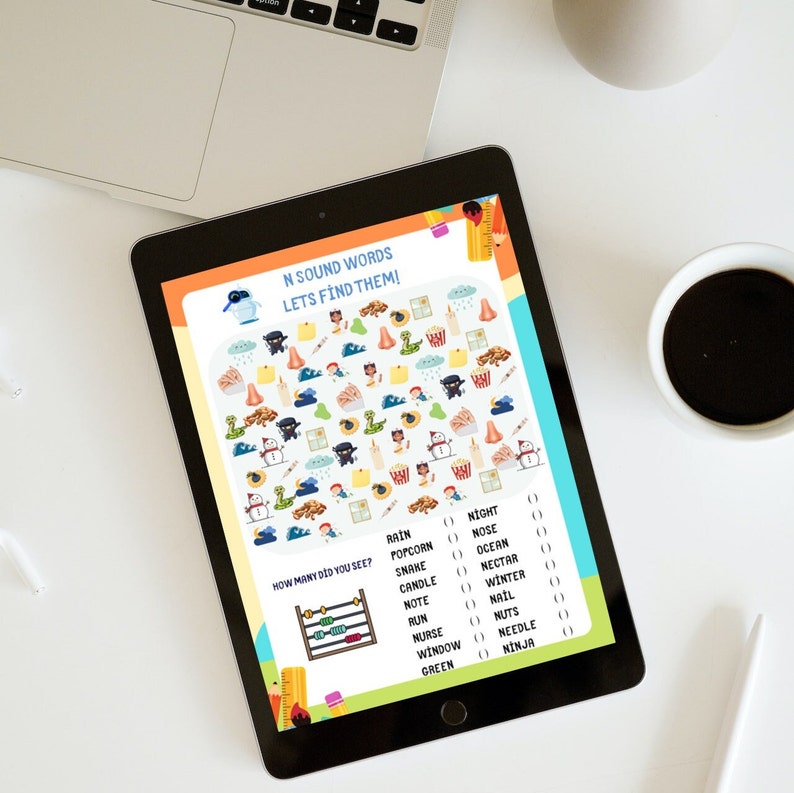 Puede incluir: Una tableta digital que muestra una hoja de actividades educativa titulada N SOUND WORDS LETS FIND THEM! La pantalla presenta una cuadr&iacute;cula de ilustraciones coloridas que incluyen ninjas, serpientes, narices y palomitas de ma&iacute;z.