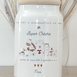 Peut inclure: Pot en céramique blanc avec un couvercle en bois, orné d'une illustration d'animaux. Le pot porte l'inscription "Super Crèche", "merci de nous aider à grandir" et le prénom "Eva".