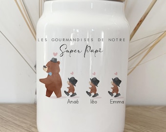 May include: White ceramic jar with a wooden lid, featuring a bear illustration with three smaller bear figures. The text "LES GOURMANDISES DE NOTRE Super Papi" and names Anaé, Léo, and Emma are printed on the jar.