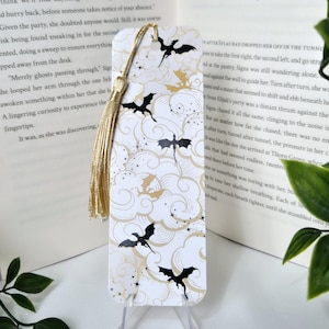 May include: A rectangular bookmark with a design of black dragons and gold clouds on a white background. It has a gold tassel at the top. The text "TWENTY-ONE" is visible in the background. The bookmark is on display.
