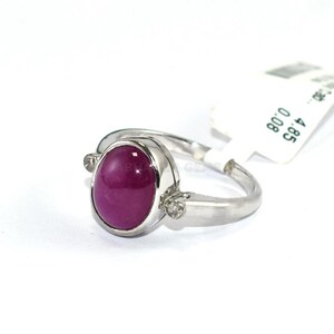 Könnte beinhalten: Ein silberfarbener Ring mit einem zentralen, ovalen, im Cabochon-Schliff geschliffenen, dunkelrosa Edelstein. Die Ringschiene ist auf beiden Seiten der Fassung mit zwei kleinen, klaren Schmucksteinen besetzt. Ein weißes Etikett ist am Ring befestigt.