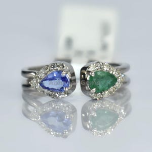 以下が含まれることがあります： 2つのシルバーリング。それぞれペアシェイプの宝石が特徴です。片方のリングには青い宝石、もう片方には緑色の宝石がセットされています。どちらも小さなクリアストーンで囲まれています。リングは白い背景に配置されています。