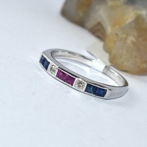 K&ouml;nnte beinhalten: Ein silberner Bandring mit einer Reihe von blauen, roten und klaren Edelsteinen.