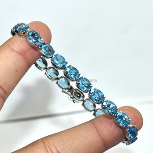 May include: A silver bracelet with a row of oval, light blue gemstones. The gemstones are set close together, forming a continuous line of colour. The bracelet is displayed against a white background.