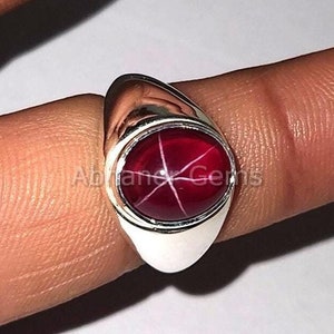 Peut inclure: Une bague en argent avec une pierre précieuse en rubis étoilé rouge. La bague est sertie dans une bélière ovale simple.