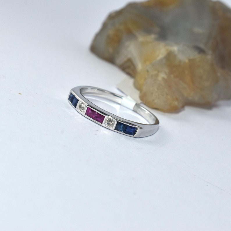 K&ouml;nnte beinhalten: Ein silberner Bandring mit einer Reihe von blauen, roten und klaren Edelsteinen.