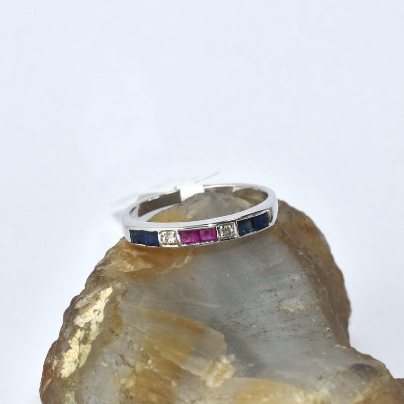 K&ouml;nnte beinhalten: Ein Wei&szlig;gold-Bandring mit einer Reihe von blauen Saphiren, rosa Rubinen und einem einzelnen Diamanten.