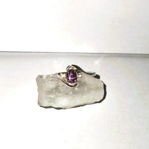 May include: A silver ring with a pink star ruby gemstone and a smaller diamond accent. The ring has a curved band.