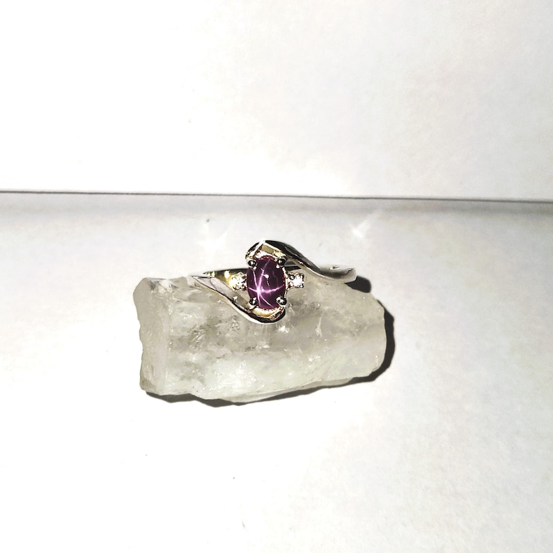 May include: A silver ring with a pink star ruby gemstone and a smaller diamond accent. The ring has a curved band.