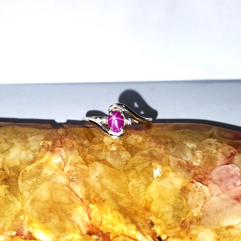 May include: A silver ring with a pink star sapphire gemstone. The ring has a delicate, curved design.