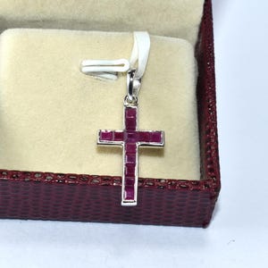 Può includere: Un ciondolo a forma di croce in argento con un'incisione di rubino rosso. Il ciondolo è in una scatola di velluto rosso.