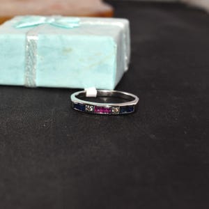 K&ouml;nnte beinhalten: Ein silberner Bandring mit drei rechteckigen Edelsteinen. Der mittlere Stein ist rosa und die beiden &auml;u&szlig;eren Steine sind blau.