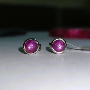 Könnte beinhalten: Ein Paar silberne Ohrstecker mit jeweils einem rosafarbenen sternförmigen Rubin.