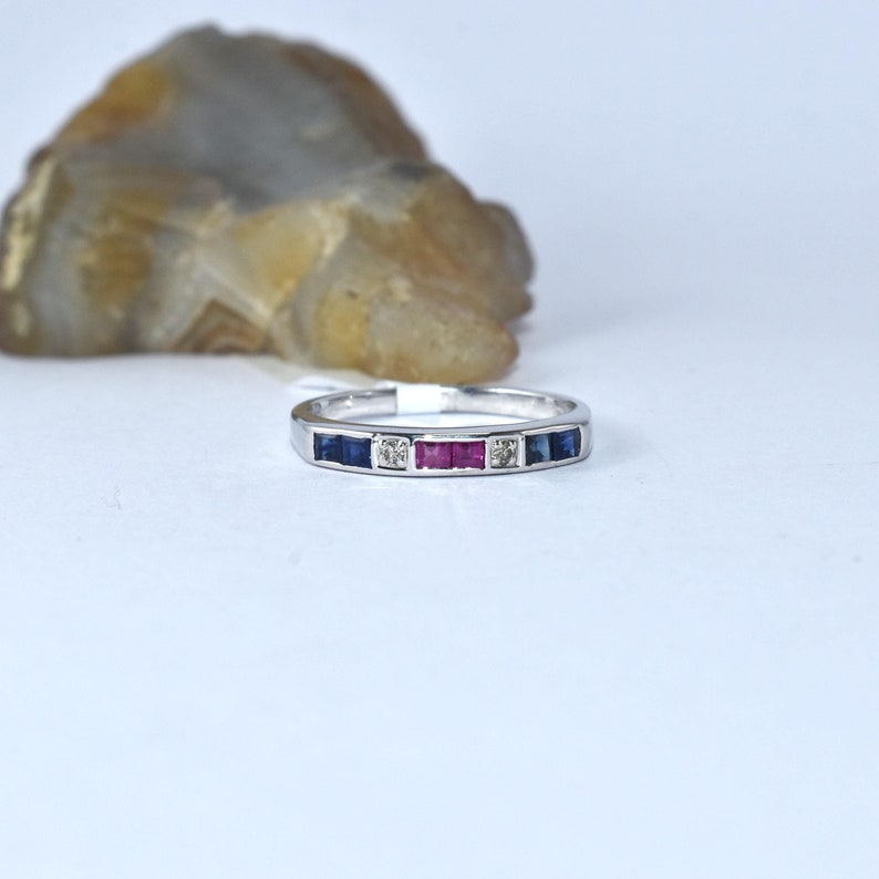 K&ouml;nnte beinhalten: Ein Silberring mit einer Reihe von blauen Saphiren, roten Rubinen und einem einzelnen Diamanten in der Mitte.