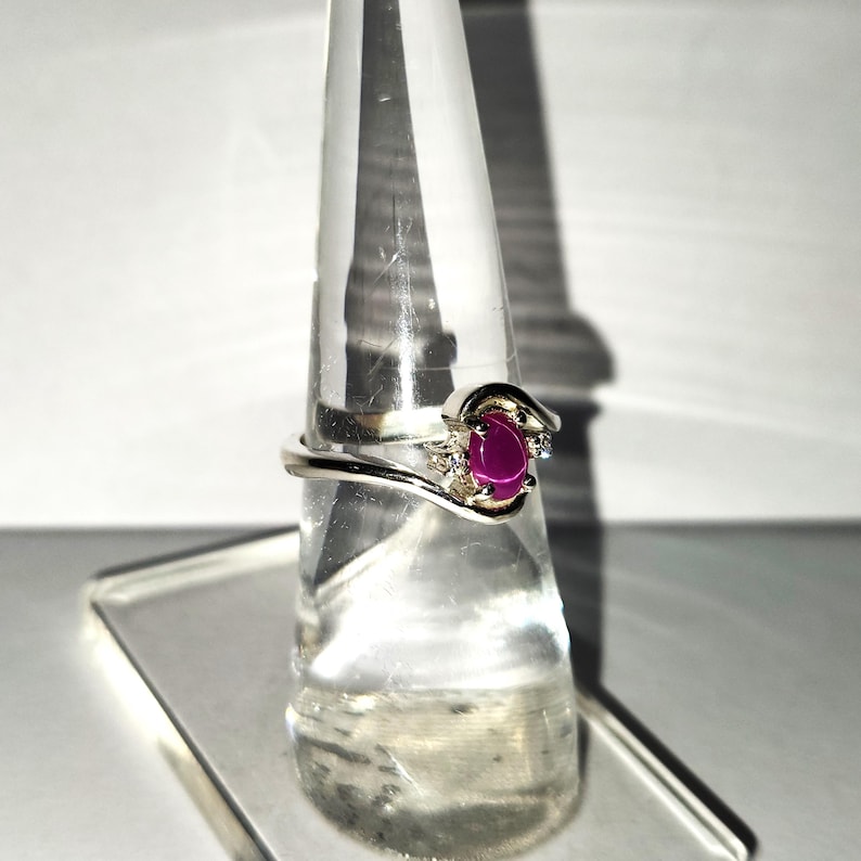 May include: A silver ring with a pink oval gemstone and two smaller clear gemstones on the band.