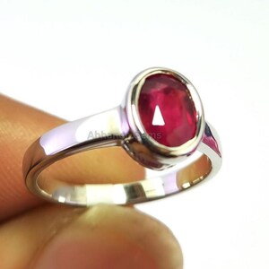 Op de afbeelding: Een zilveren ring met een grote, ovaal geslepen robijn edelsteen. De robijn heeft een helderrode kleur en is gezet in een gepolijste zilveren band. De ring wordt getoond tegen een witte achtergrond.