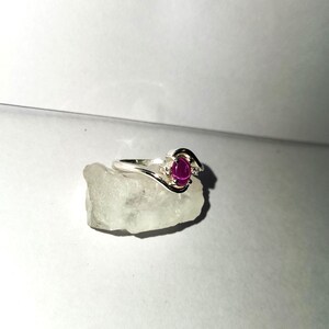 May include: A silver ring with a pink oval gemstone and two smaller clear gemstones.
