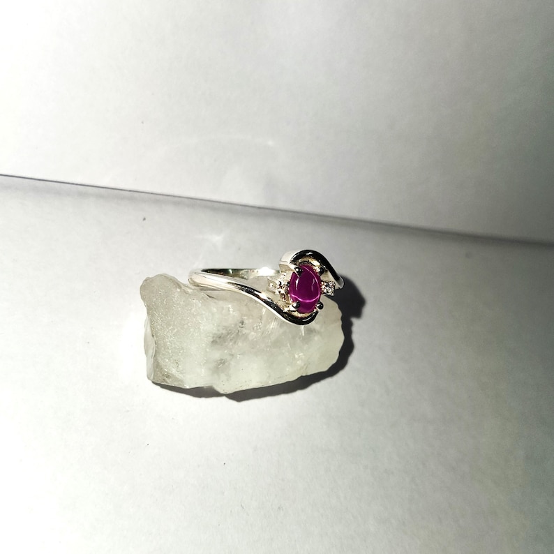 May include: A silver ring with a pink oval gemstone and two smaller clear gemstones.