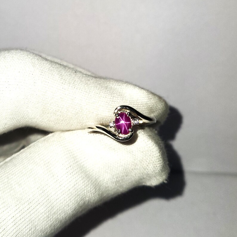 May include: A silver ring with a pink star ruby gemstone and two smaller diamonds. The ring has a curved band.