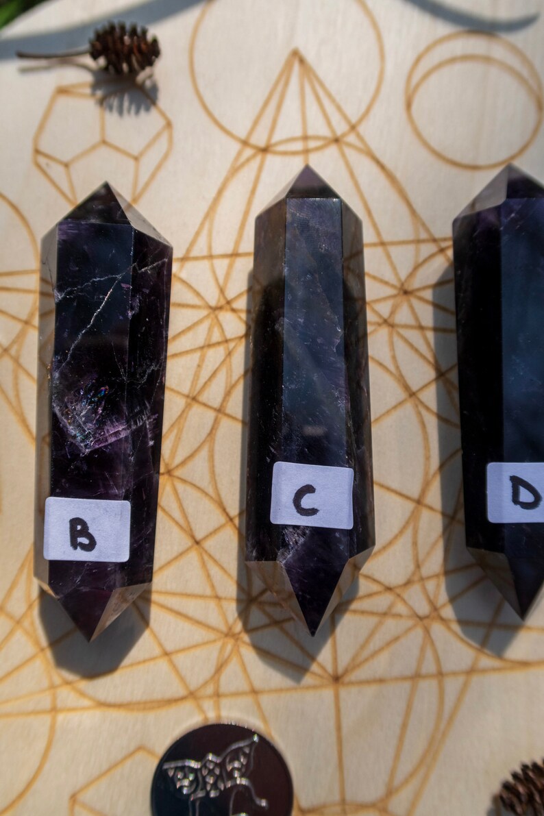 May include: Three black amethyst crystal points with labels "B", "C", and "D" arranged on a wooden board with a geometric pattern.