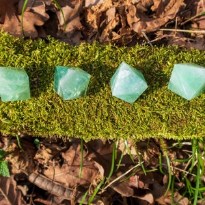 May include: Five green fluorite pyramid crystals arranged in a row on a bed of moss.
