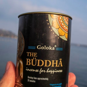 May include: A black metal tin of incense with a gold lid. The tin has a colorful mandala design and the text "Goloka The Buddha incense for happiness". The text "Burning time approximately 20 minutes" is also on the tin. The quote "There is no path to happiness, happiness is the path" is printed on the tin in blue text. The Buddha (Mette Su"