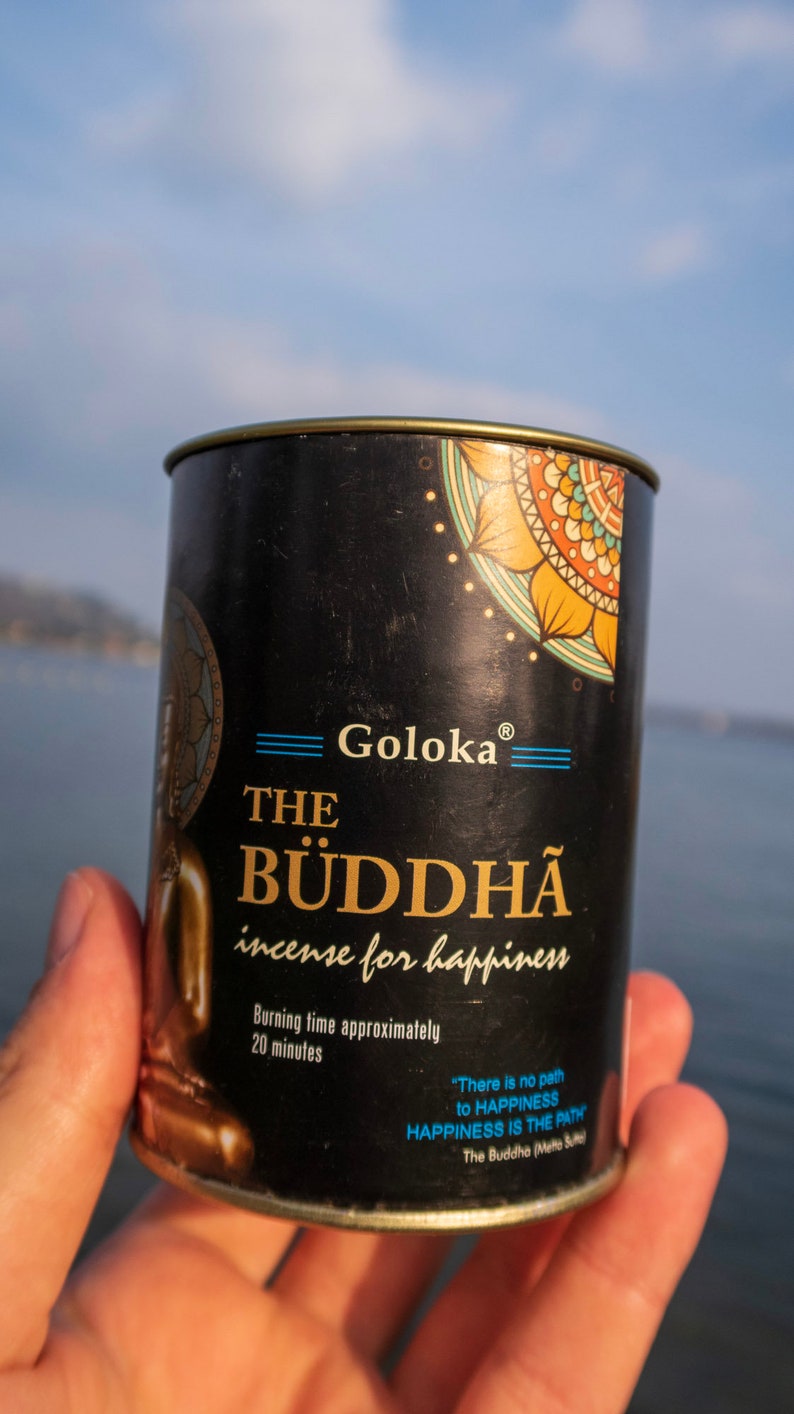 May include: A black metal tin of incense with a gold lid. The tin has a colorful mandala design and the text "Goloka The Buddha incense for happiness". The text "Burning time approximately 20 minutes" is also on the tin. The quote "There is no path to happiness, happiness is the path" is printed on the tin in blue text. The Buddha (Mette Su"