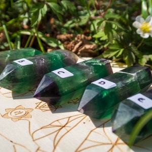 May include: Five green and purple fluorite crystal points, labeled A through E, arranged on a wooden surface with a carved design.