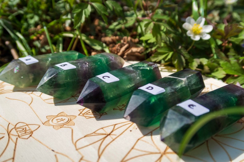 May include: Five green and purple fluorite crystal points, labeled A through E, arranged on a wooden surface with a carved design.