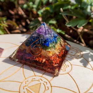 May include: A seven-chakra crystal pyramid with a copper wire spiral. The pyramid is made of clear resin and contains small pieces of amethyst, sodalite, blue lace agate, green aventurine, citrine, carnelian, and red jasper.