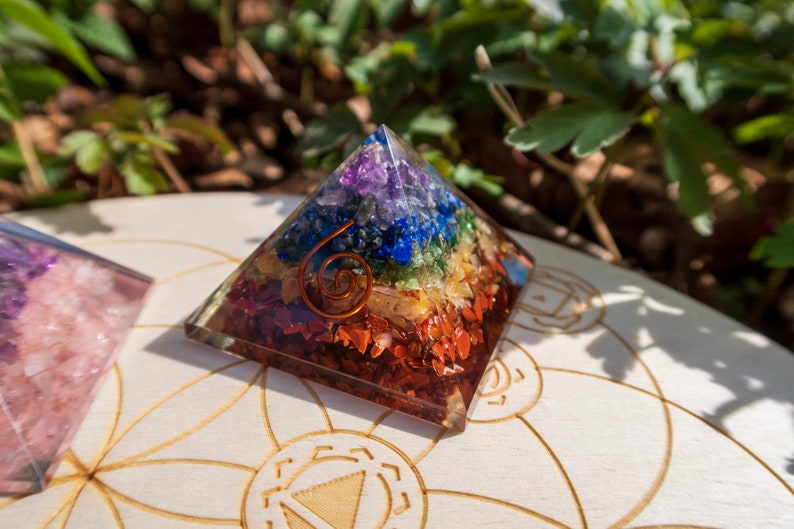 May include: A seven-chakra crystal pyramid with a copper wire spiral. The pyramid is made of clear resin and contains small pieces of amethyst, sodalite, blue lace agate, green aventurine, citrine, carnelian, and red jasper.