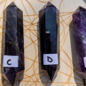 May include: Three black and purple crystal wands on a wooden surface with a geometric pattern. The wands are labeled C, D, and E.