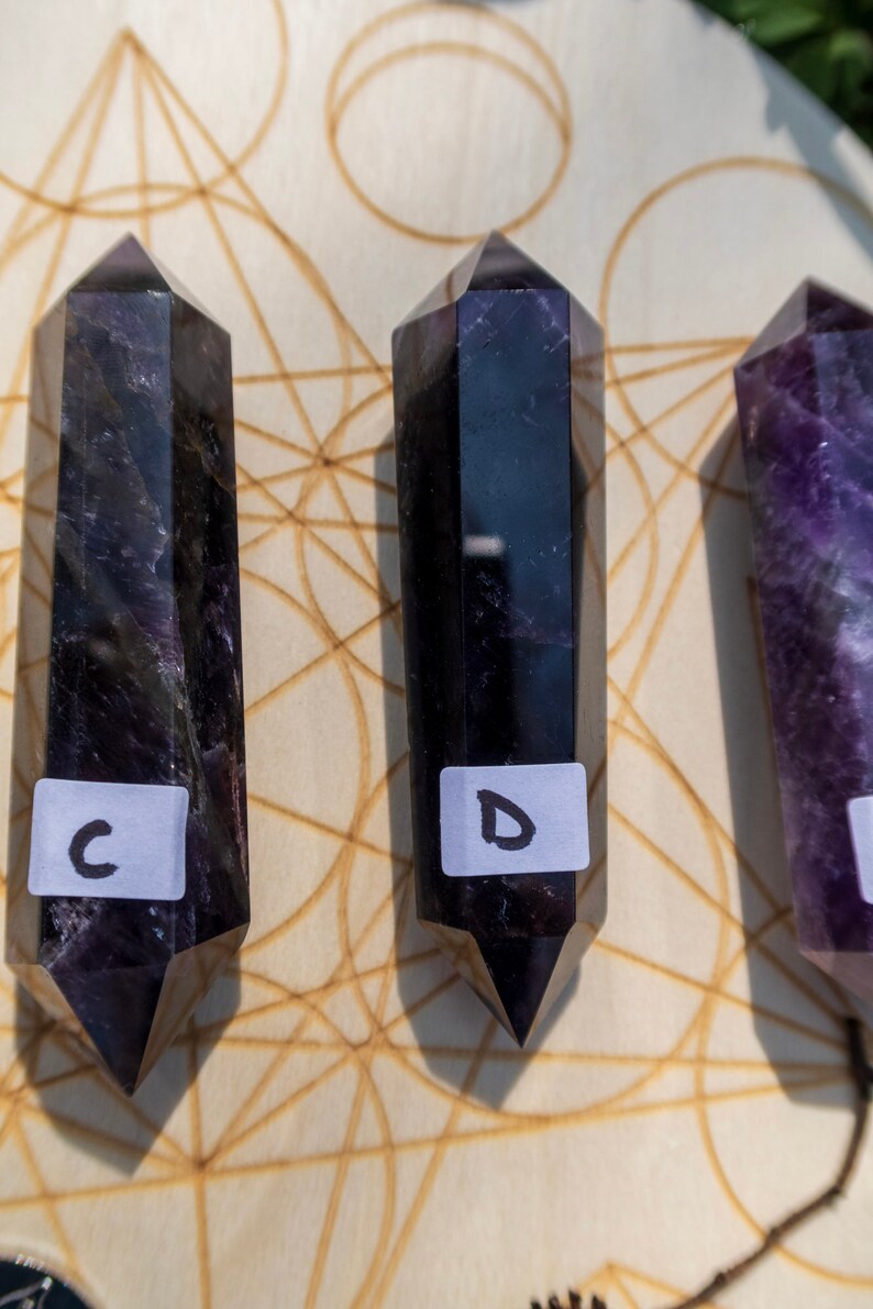 May include: Three black and purple crystal wands on a wooden surface with a geometric pattern. The wands are labeled C, D, and E.