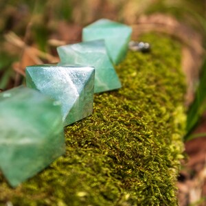 May include: Five green, faceted, crystal pyramids arranged in a row on a bed of moss. The crystals are translucent and have a light green colour.