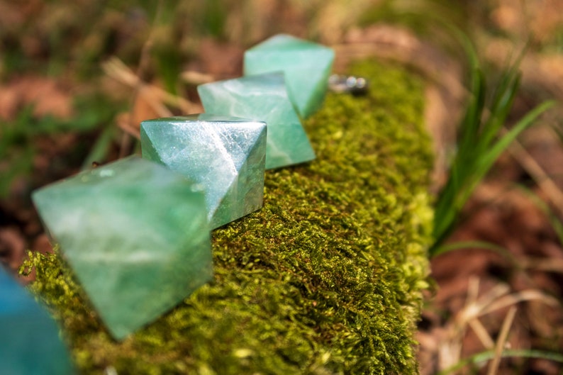 May include: Five green, faceted, crystal pyramids arranged in a row on a bed of moss. The crystals are translucent and have a light green colour.
