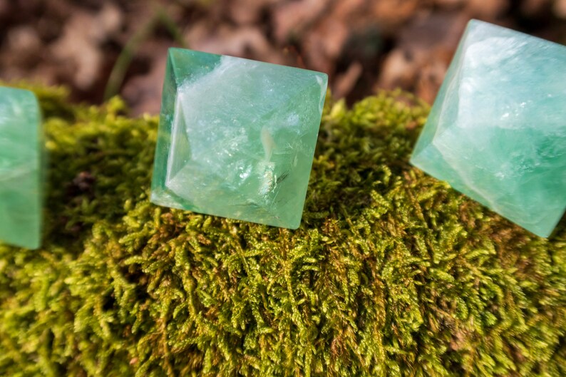 May include: Three green fluorite pyramid crystals on a bed of moss. The crystals are translucent and have a slight shimmer.