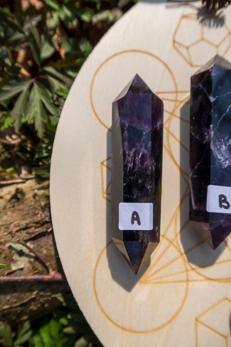May include: Two dark purple amethyst crystal points on a wooden board with a geometric design. The points are labeled "A" and "B".
