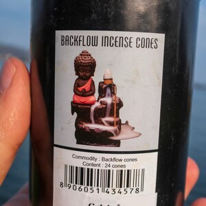 May include: A black metal tin with a gold lid containing 24 backflow incense cones. The label features a small Buddha statue and the text "Backflow Incense Cones" and "Goloka".