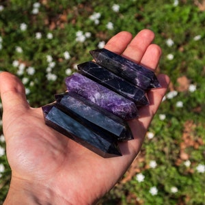 May include: Five amethyst crystal points, each with a pointed tip and a smooth, polished surface. The crystals are arranged in a stack, with the largest at the bottom and the smallest at the top. The crystals are a deep purple color with hints of black.