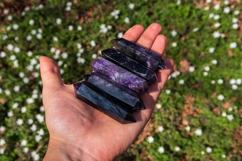 May include: Five amethyst crystal points, each with a pointed tip and a smooth, polished surface. The crystals are arranged in a stack, with the largest at the bottom and the smallest at the top. The crystals are a deep purple color with hints of black.