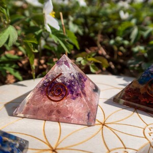 May include: Two crystal pyramids with a copper wire spiral design. The pyramid on the left is pink and purple, while the pyramid on the right is multi-coloured.