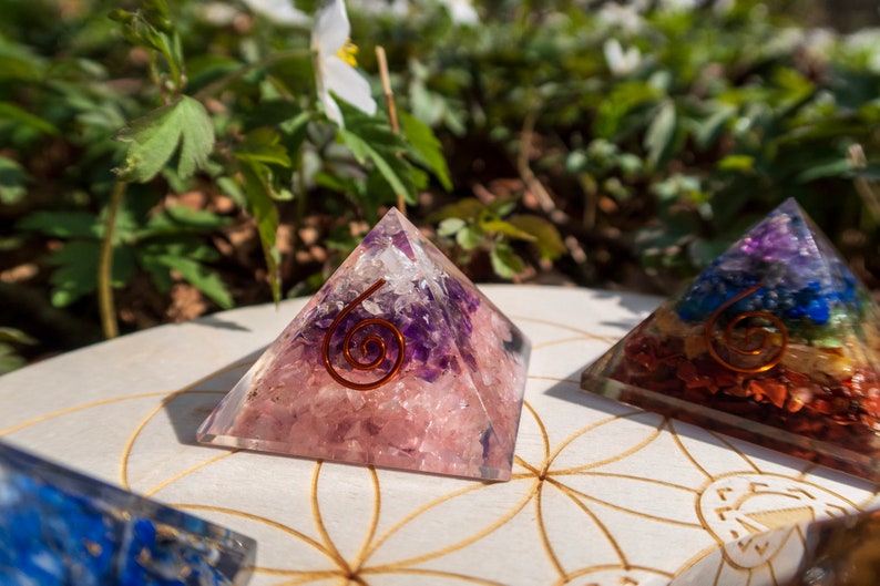 May include: Two crystal pyramids with a copper wire spiral design. The pyramid on the left is pink and purple, while the pyramid on the right is multi-coloured.