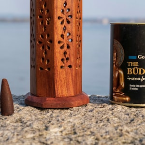 May include: Two brown incense cones next to a wooden incense burner and a black tin of Goloka The Buddha incense for happiness. The tin has a gold Buddha image and text that says "Burning time approximately 20 minutes".