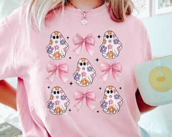 May include: A pale pink sweatshirt with a repeating pattern of floral ghosts and pink bows. The ghosts have orange, purple, and white flowers. The word "BLOSSOM" is printed in the bottom right corner.