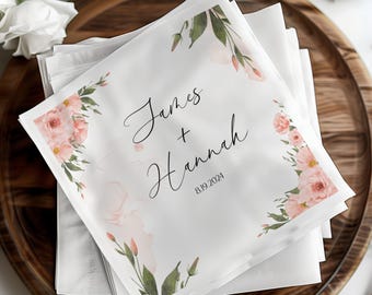May include: White wedding napkins with a floral design in shades of pink and green. The napkins feature the names "James + Hannah" and the date "8.19.2024".
