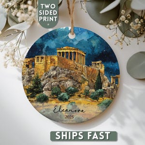 May include: Round ceramic ornament featuring a watercolor painting of the Parthenon in Athens, Greece, under a starry night sky. The ornament has a two-sided print and includes the name "Eleanora" and the year "2025".