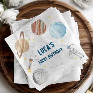 May include: White napkins with a space-themed design featuring planets, stars, and an astronaut. The text "LUCA'S FIRST BIRTHDAY" is printed in blue.