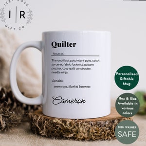 May include: White ceramic mug with a black design that reads "Quilter" and defines the word as "The unofficial patchwork poet, stitch sorcerer, fabric fusionist, pattern puzzler, cosy quilt constructor, needle ninja." The mug also says "See also: seam sage, blanket baroness" and has the name "Cameron" printed on the bottom. The mug is sitting on a wooden surface.