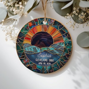 May include: Round ornament with a stained glass design featuring a sunset over water. The ornament has a wooden frame and a jute string for hanging. The text "Sophia, Cleveland, Ohio, April 08, 2024" is displayed on the bottom.